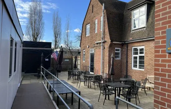 Outdoor seating area with tables and chairs on a paved courtyard beside a brick building on a sunny day.