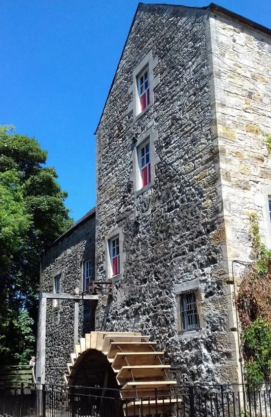 Stone-built historic tower building with red-framed windows and wooden entrance steps, set against clear blue sky with green foliage.