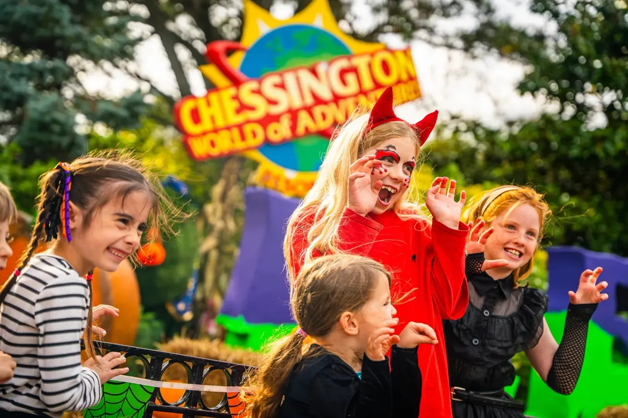 Children in Halloween costumes, including devil horns and face paint, smiling at Chessington World of Adventures theme park.