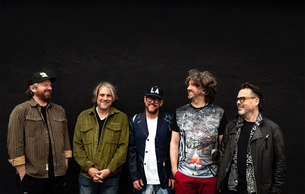 Five men standing together against a black background, smiling at the camera.