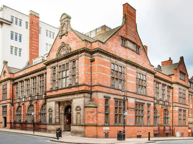 Historic red-brick Victorian building with distinctive chimneys and arched windows, viewed from street level.