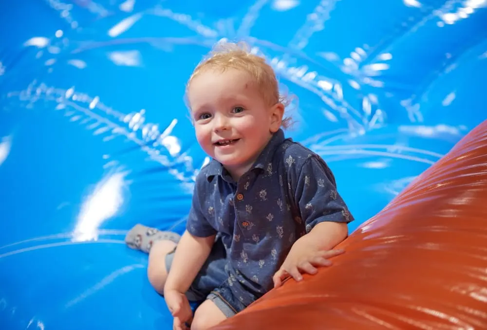 Young child playing on a large red inflatable structure in a ball pit with blue background.