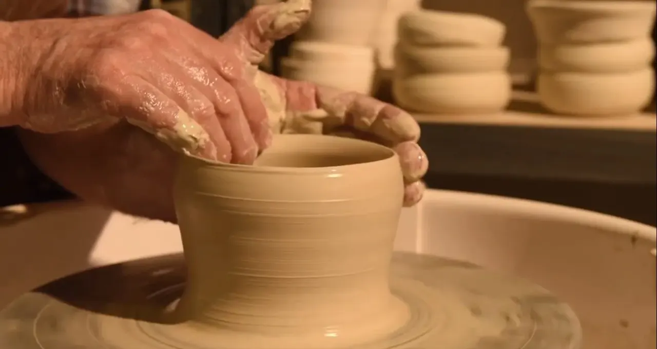Hands shaping wet clay on a potter's wheel during a pottery lesson.