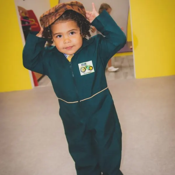 Young child wearing a dark blue jumpsuit and patterned headscarf, posing indoors at a play venue.