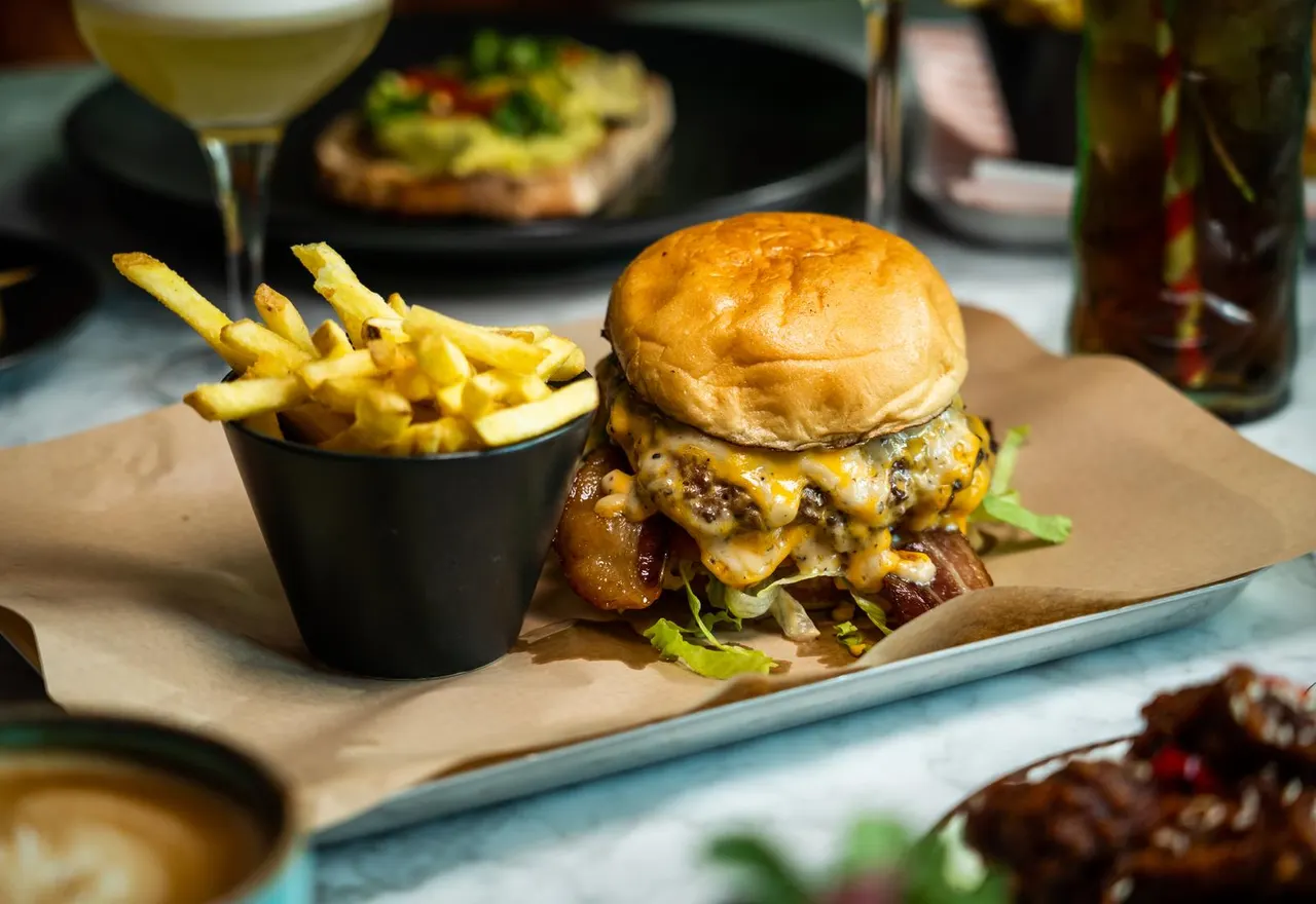 Cheeseburger with melted cheese and bacon served with chips, accompanied by wine and cocktails.