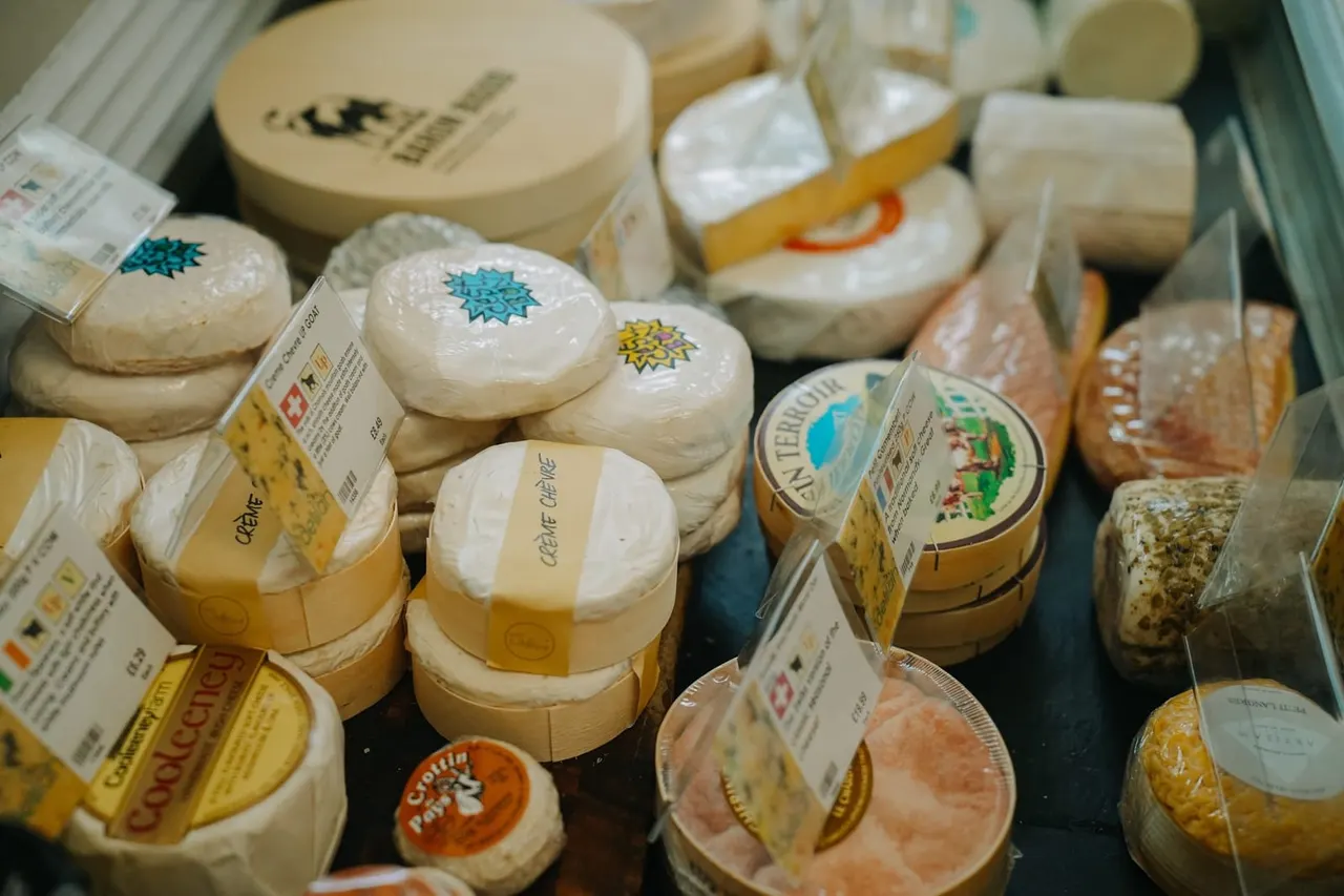 Assorted fresh cheeses and cured meats displayed in a refrigerated case with product labels and packaging.