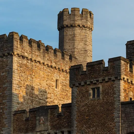 Stone castle with crenellated towers and walls bathed in golden sunlight against a clear blue sky.