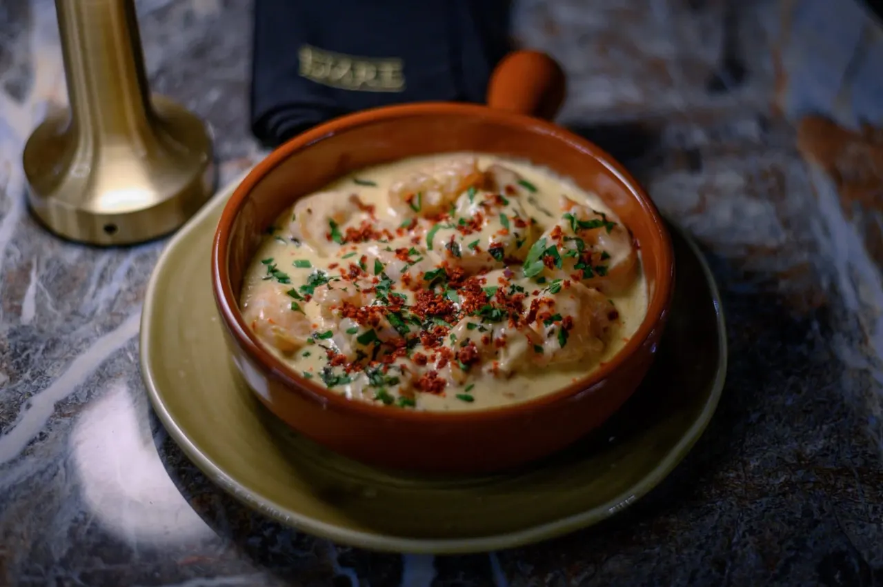Creamy hummus dip garnished with paprika and parsley in a terracotta bowl on a plate.