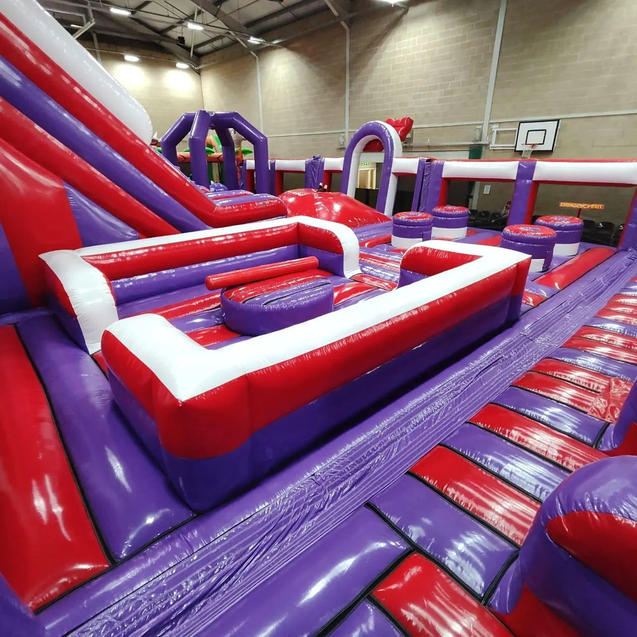 Indoor play area with inflatable obstacle courses and activities in red, purple and white.