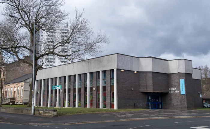 Modern brick library building with tall windows and entrance doors on an urban street with bare trees.