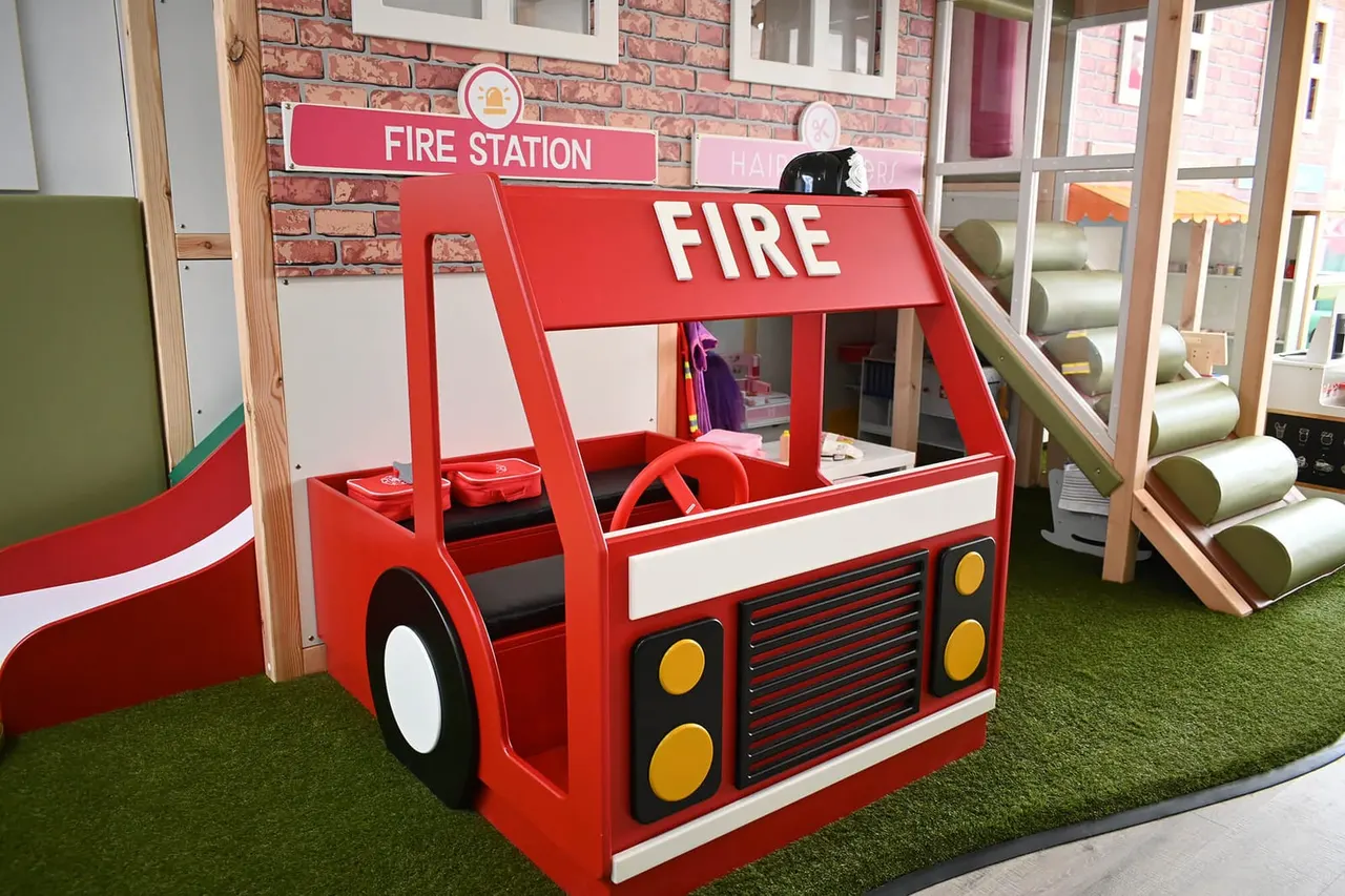 Red fire engine play structure in an indoor soft play area with slide and other equipment visible.