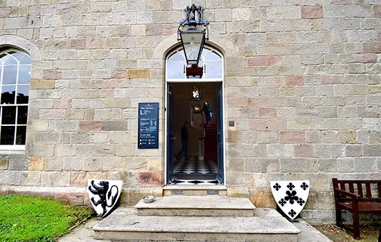 Stone castle entrance with wooden door, heraldic shields displayed either side, and a suit of armour visible inside the doorway.