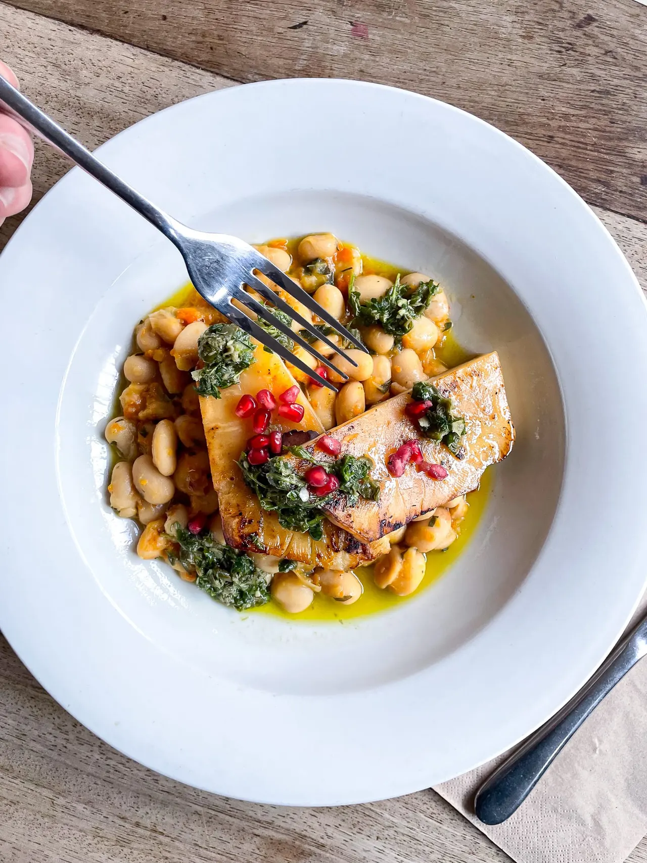 Seared fish fillet with chickpeas, kale and pomegranate seeds on a white plate.