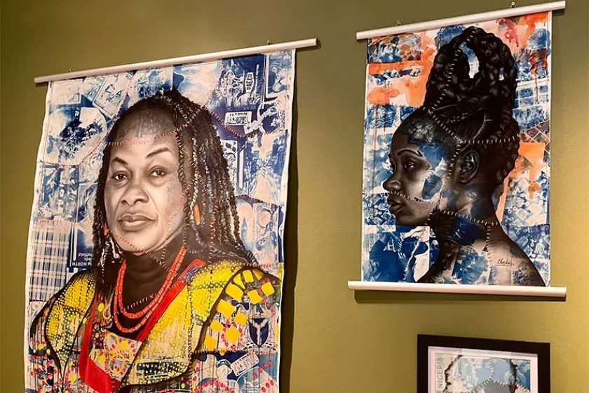 Two large portrait artworks hanging on a yellow wall, featuring stylised faces of Black women with decorative patterns and collaged backgrounds in blue, orange and yellow tones.