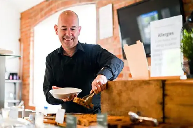 Man in black shirt serving food onto a plate at a restaurant counter.
