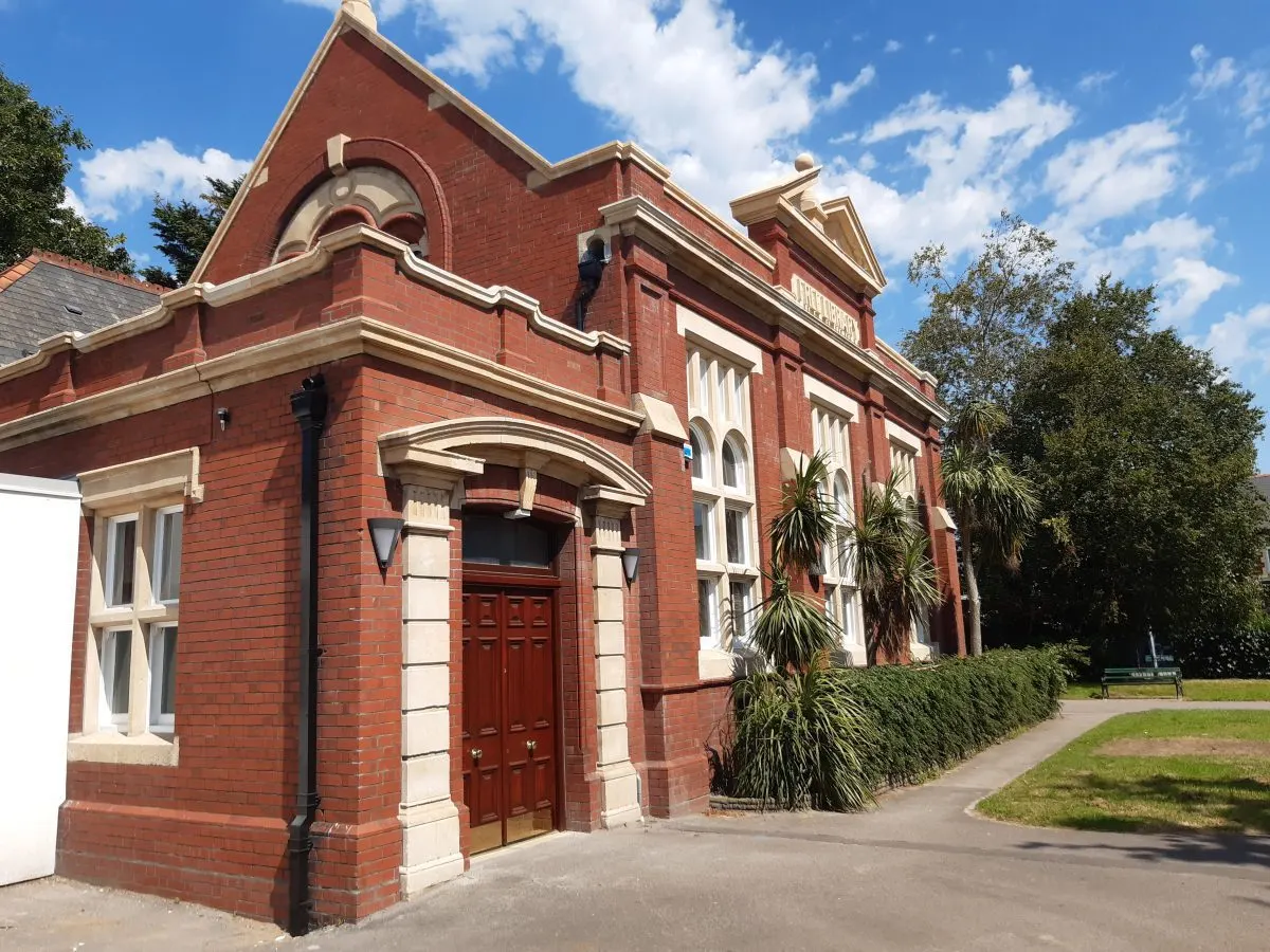Victorian red brick building with cream stone detailing, set in a landscaped garden on a sunny day.
