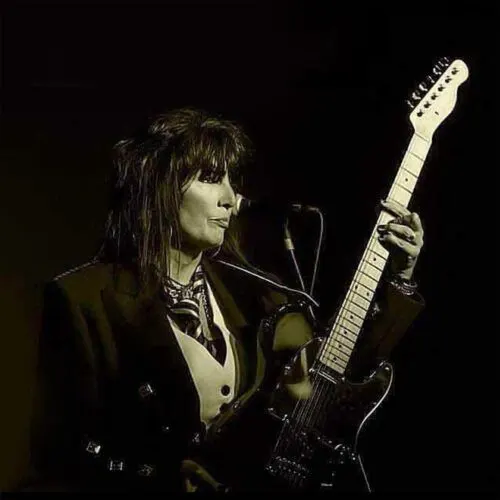 Musician performing with electric guitar and microphone on stage.