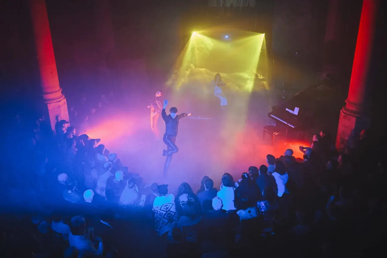 Live music performance with crowd dancing under vibrant coloured stage lighting in an indoor venue.
