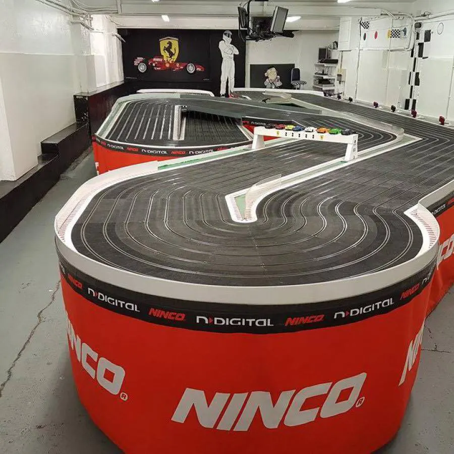 Slot car racing track with two oval circuits, red barriers, and Ferrari and racing memorabilia on walls.