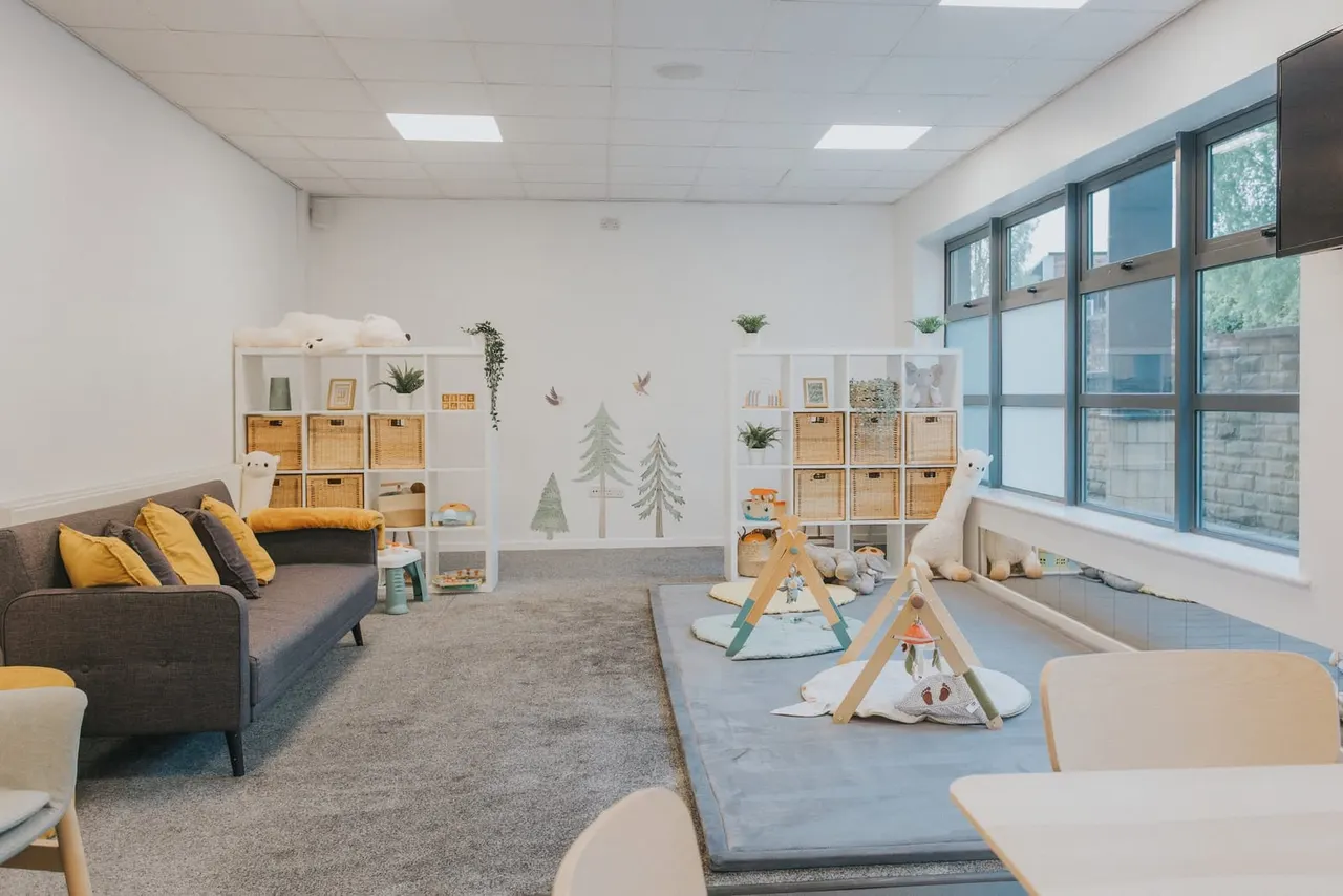 Modern indoor play area with sofa, storage units, play tents, and woodland-themed wall decoration for young children.