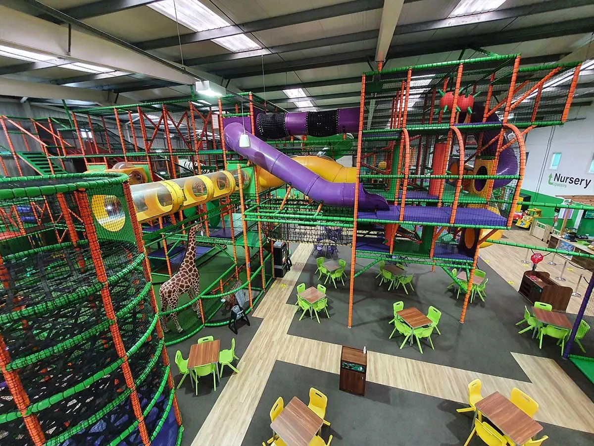 Indoor play centre with multi-coloured climbing structures, slides, and soft play equipment, with seating areas below.