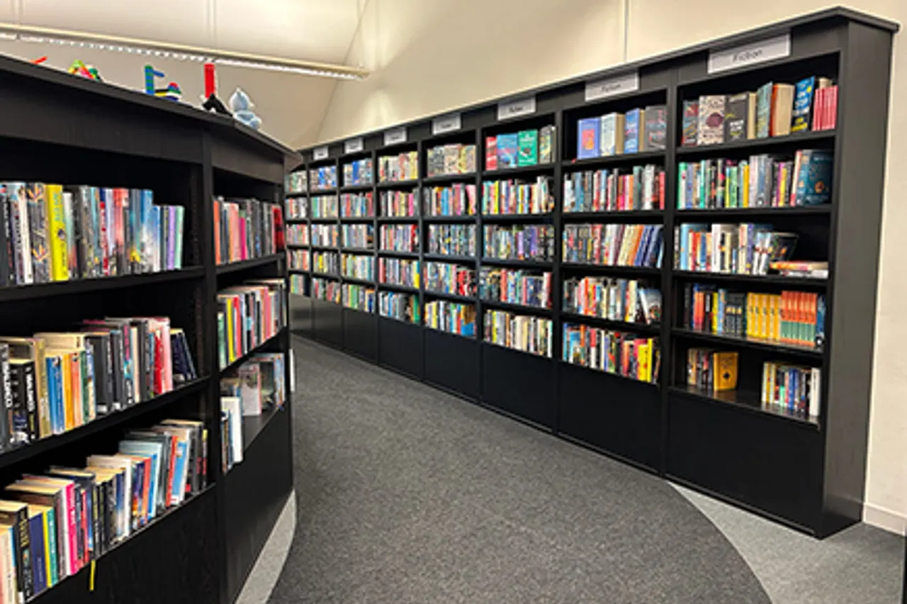 Library shelving with extensive collection of books and DVDs organised on black wall-mounted units.