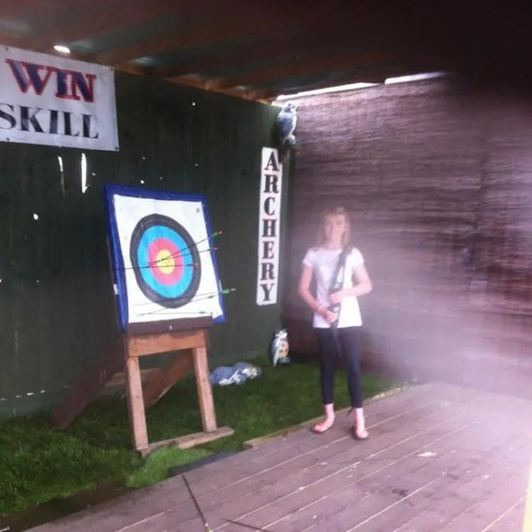 Person holding a bow and arrow aiming at an archery target inside an indoor activity venue.