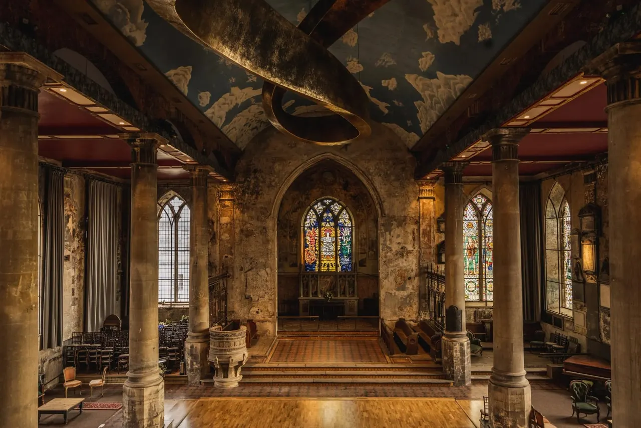 Interior of a grand Gothic-style chapel with soaring columns, ornate ceiling, stained glass windows and worn stone walls.