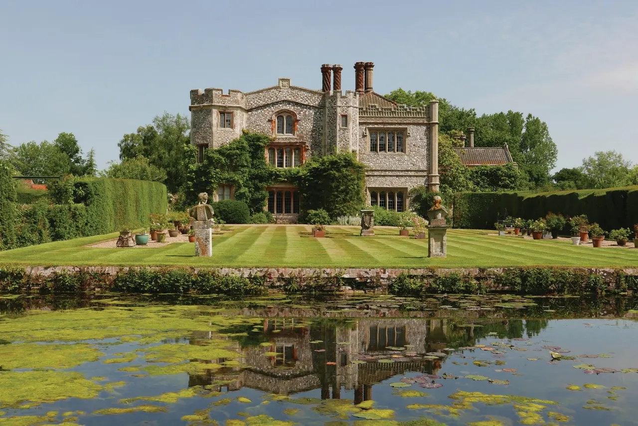 Stone mansion with manicured lawns and terracotta urns, reflected in a pond with water lilies.