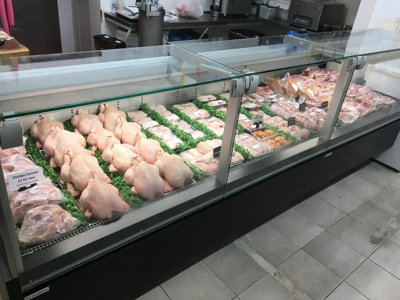 Refrigerated butcher's counter displaying various cuts of poultry and meat for sale.