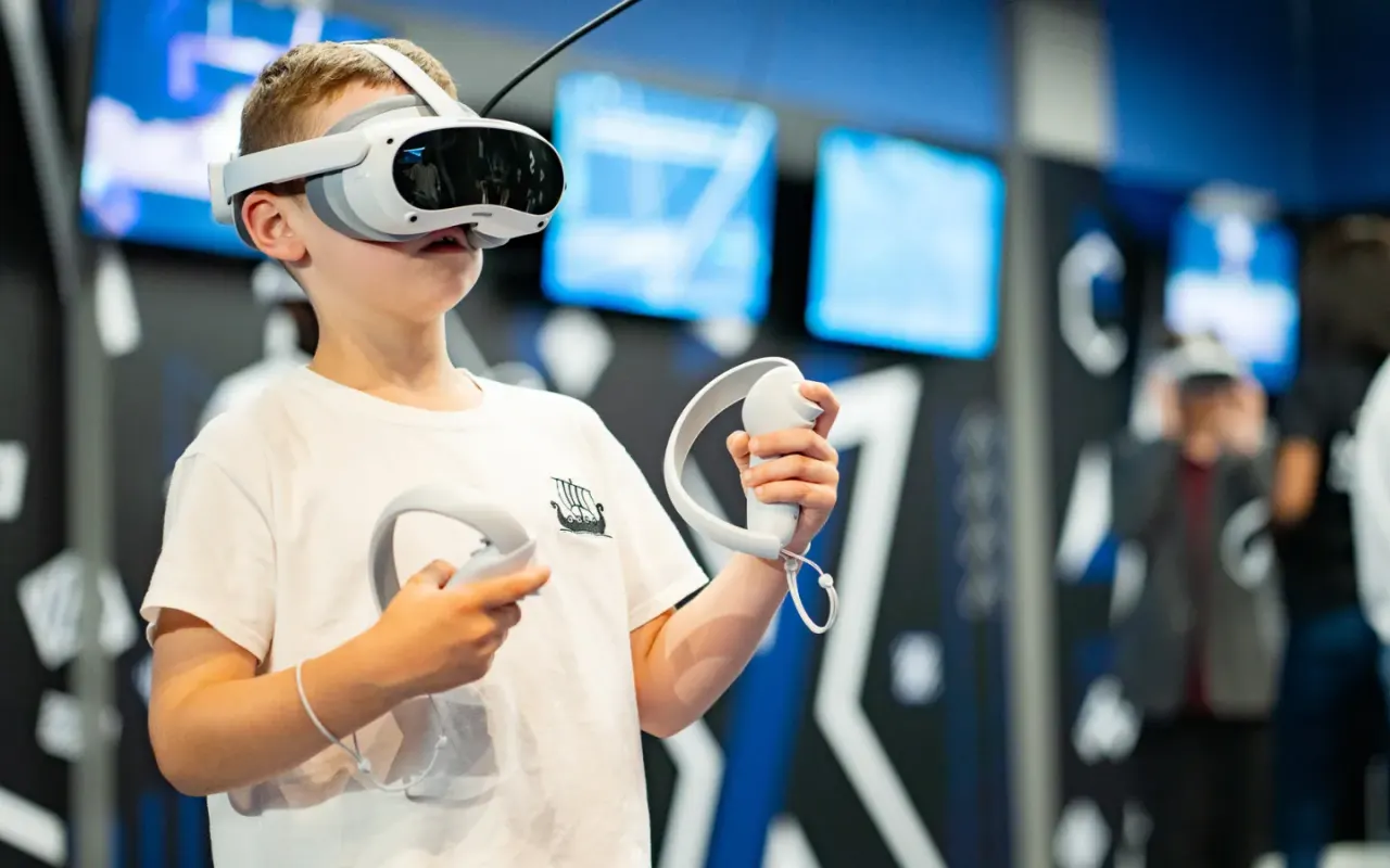 Child wearing a virtual reality headset and holding controllers whilst playing an immersive VR game in an arcade facility.