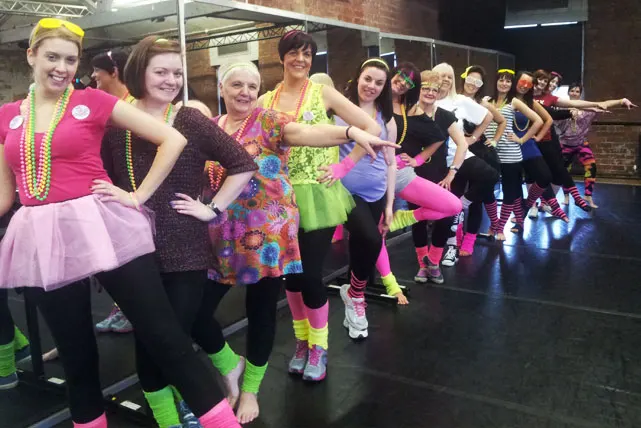 Group of people in bright neon and colourful costumes dancing together in a studio.