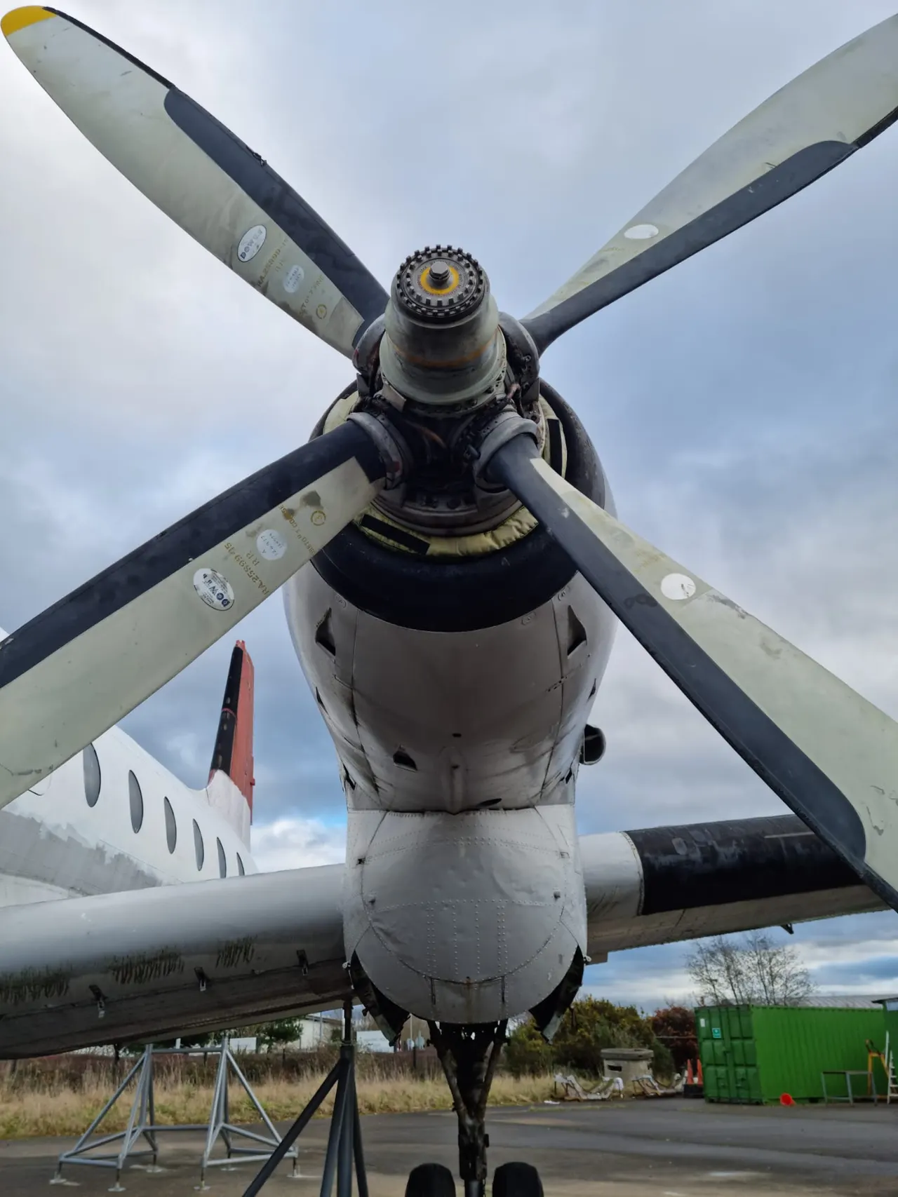 Close-up view of a vintage aircraft's four-bladed propeller and engine cowling from directly below, against a cloudy sky.