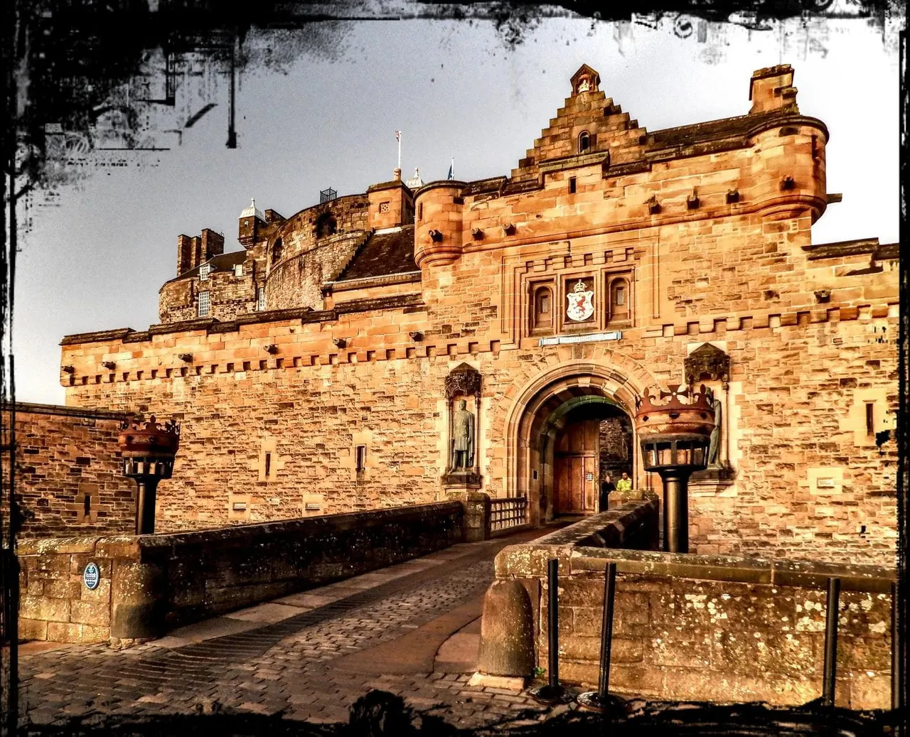 Historic sandstone castle with crenellated walls and turrets, viewed from a cobbled courtyard approach.