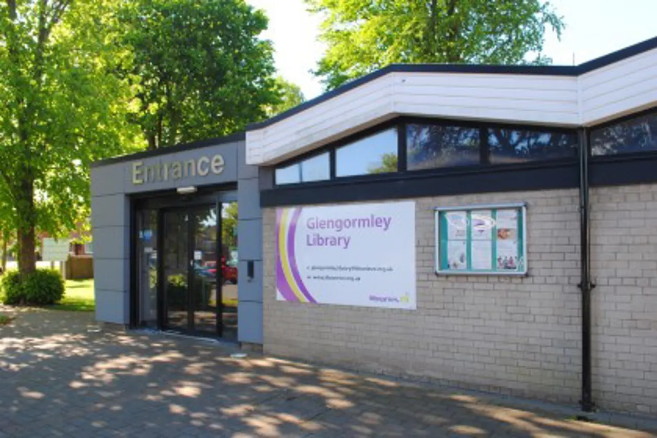 Modern single-storey library building with entrance, surrounded by mature trees on a sunny day.