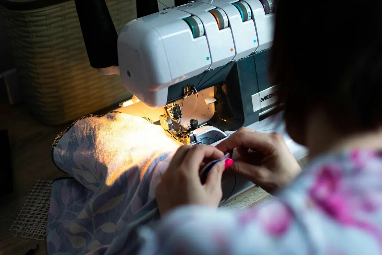 A person uses an embroidery machine to stitch a design onto fabric whilst seated at the machine.