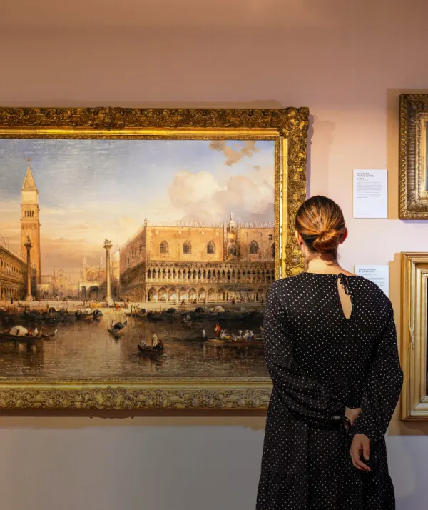 Woman viewing a large classical painting of a Venetian palace and waterfront scene in a gallery setting.