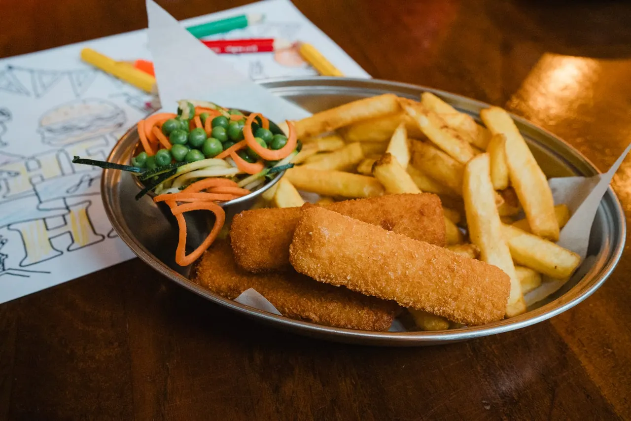 Breaded fish fillets served with chips and vegetable garnish on a plate at a dining table.