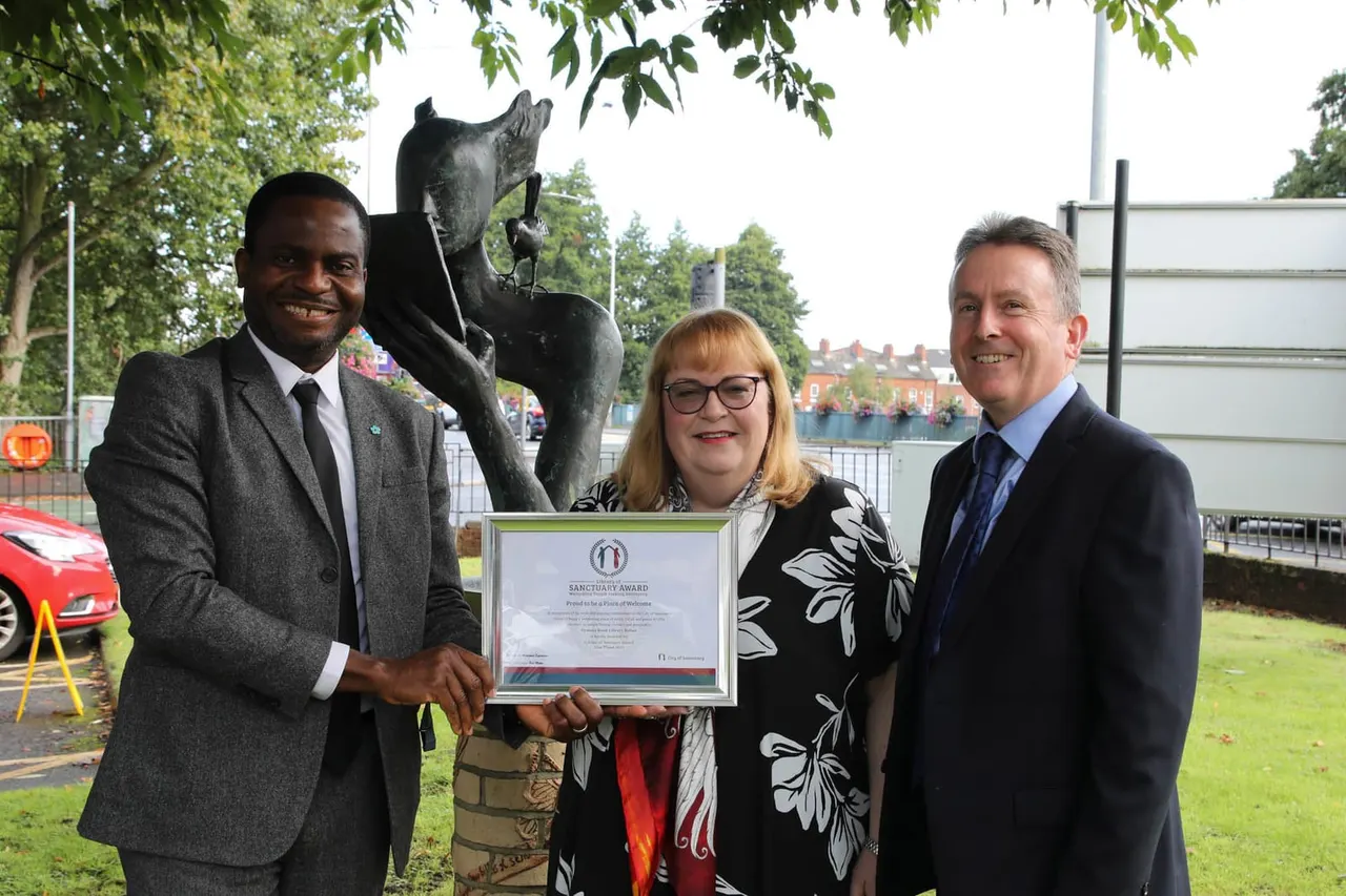 Three people in business attire hold a framed certificate next to a bronze horse sculpture by a waterside venue.