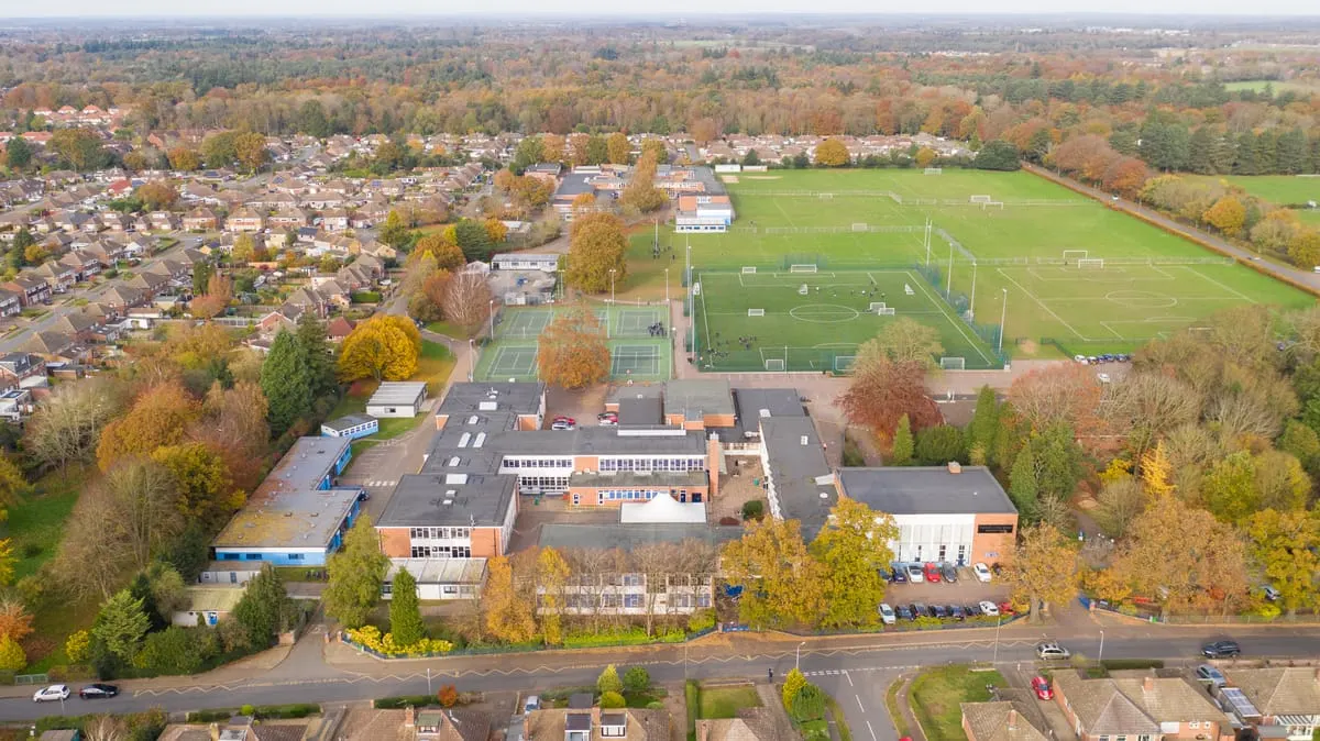 Aerial view of a sports complex with multiple football pitches, tennis courts and school buildings surrounded by autumn trees and suburban housing.