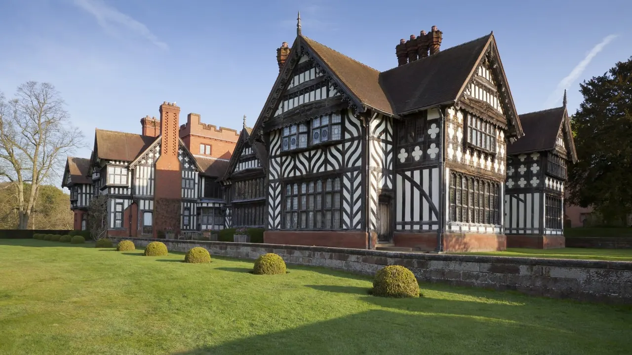 Tudor and Jacobean timber-framed manor house with decorative black and white patterning, set behind manicured lawns with topiary hedges.