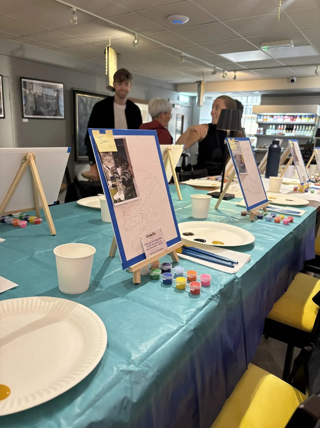 People participating in a guided art workshop with easels, paints and drawing materials at a table.