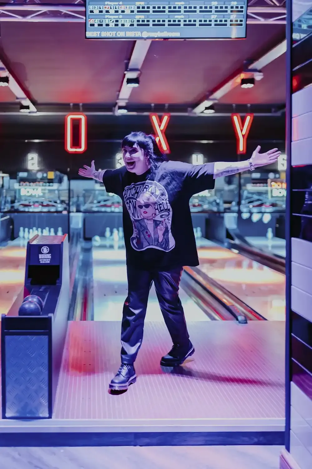 Person celebrating with arms outstretched on a bowling lane under neon signage at an entertainment venue.
