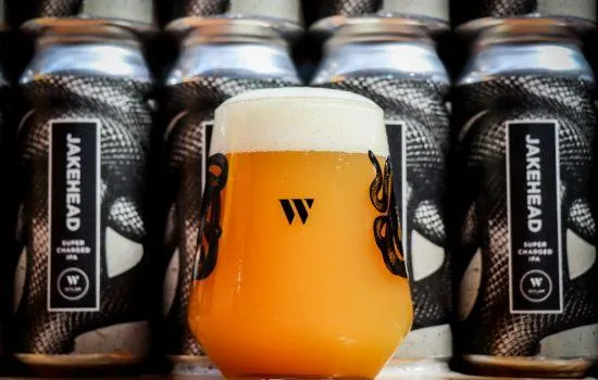 A glass of golden-orange beer surrounded by four dark canned beers from Wylam Brewery.