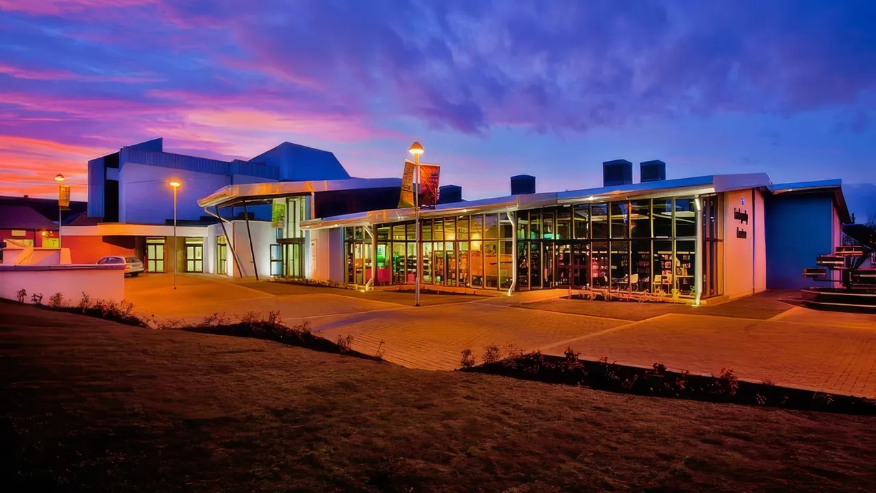 Modern leisure building illuminated at dusk with colourful lighting, situated on a sandy beach at twilight.