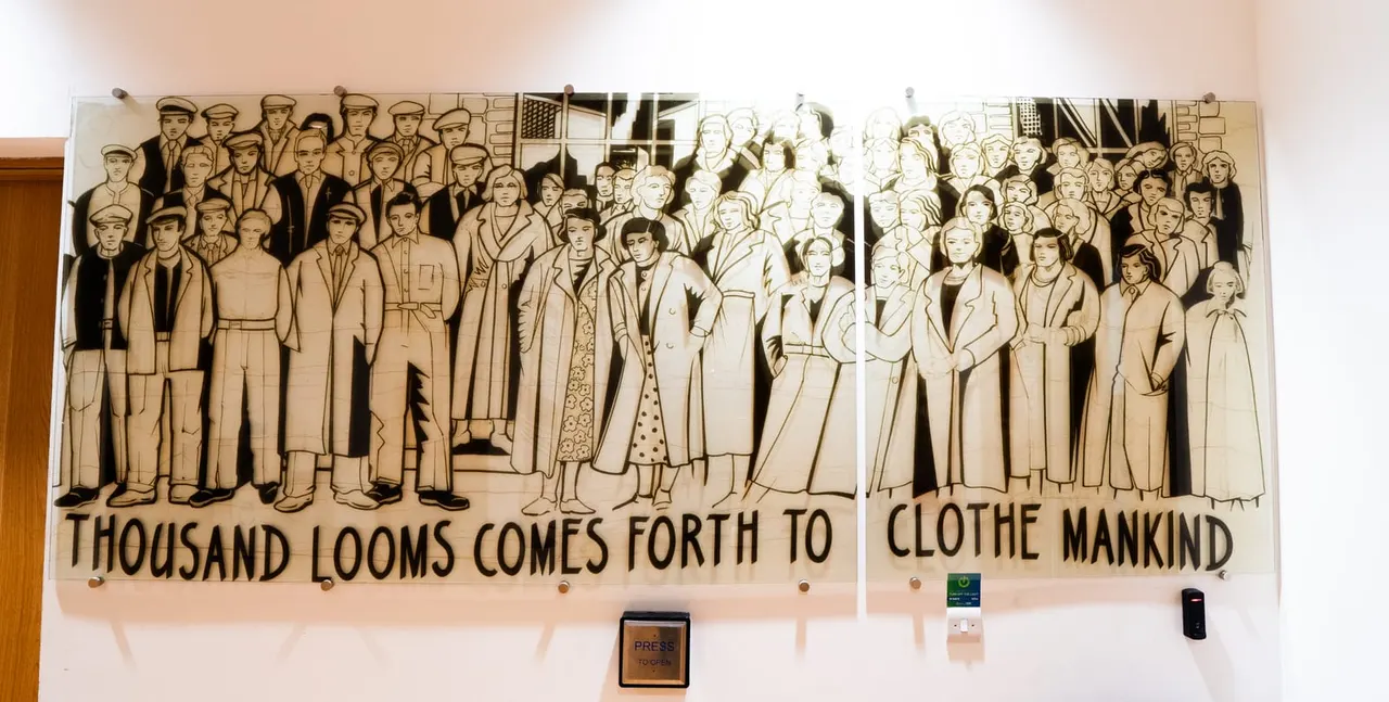 Large relief artwork depicting crowds of people in period clothing with text reading "Thousand Looms Comes Forth to Clothe Mankind".