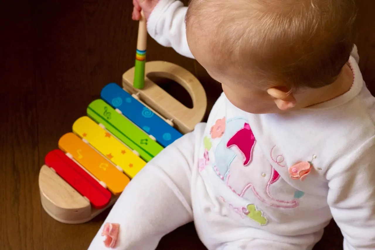Toddler playing with a colourful wooden xylophone toy during a sensory activity.