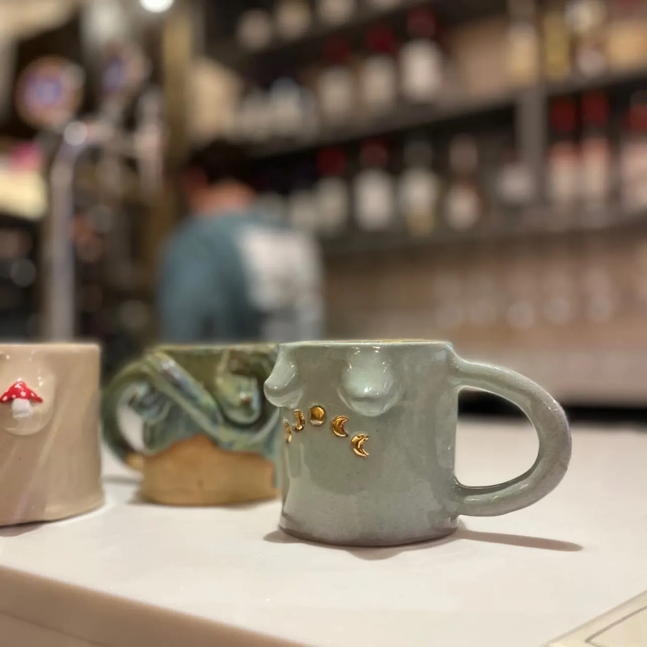 Decorative ceramic mugs displayed on a white counter in a pottery studio shop.