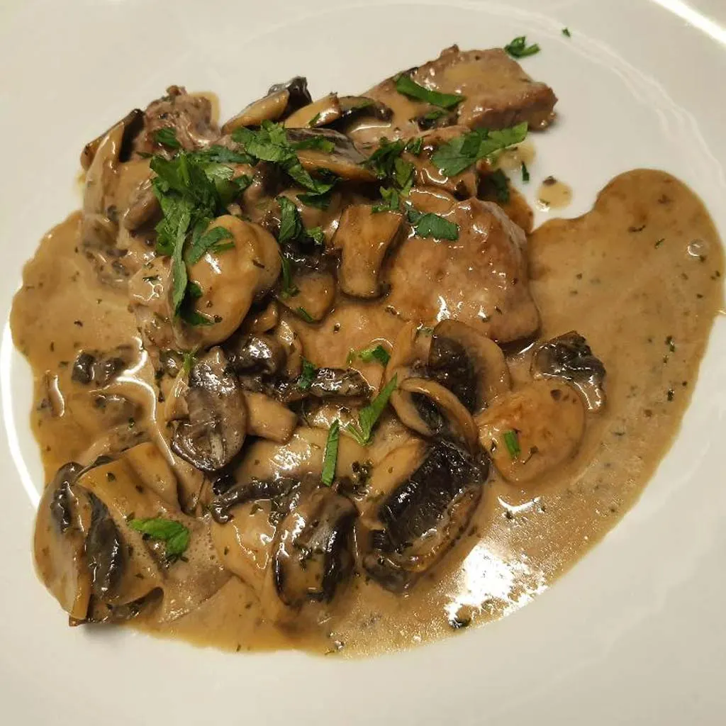 Beef stroganoff with mushrooms, soured cream sauce and fresh parsley on white plate.