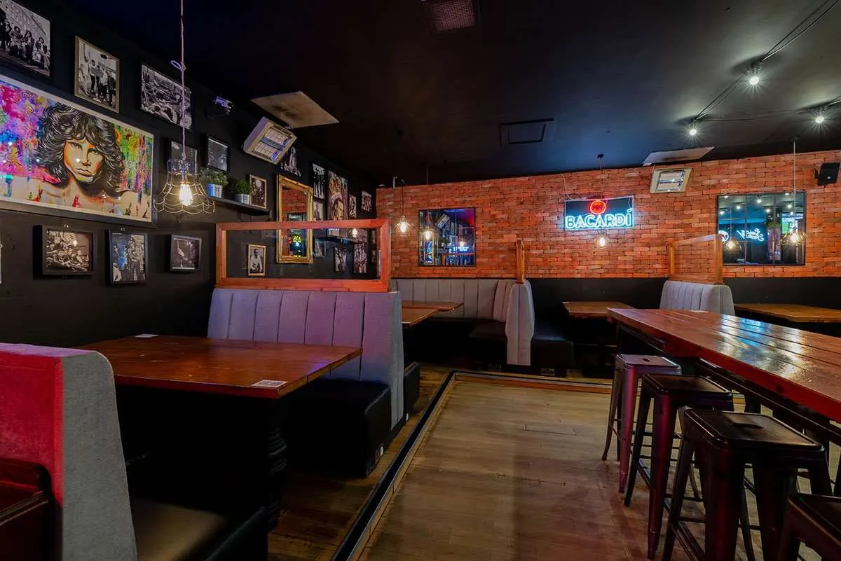 Interior of a nightclub with booth seating, wooden tables, exposed brick walls, neon signs, and framed artwork.